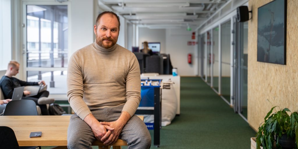 Avoin työtila, jossa pöytiä, työskentelyalueita ja istuva henkilö etualalla.