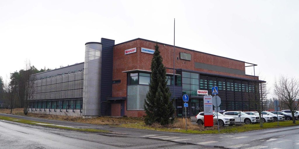 Toimistokiinteistö pihapiirin puolelta, rakennuksen julkisivussa yritysopaste ja parkkialue edessä.
