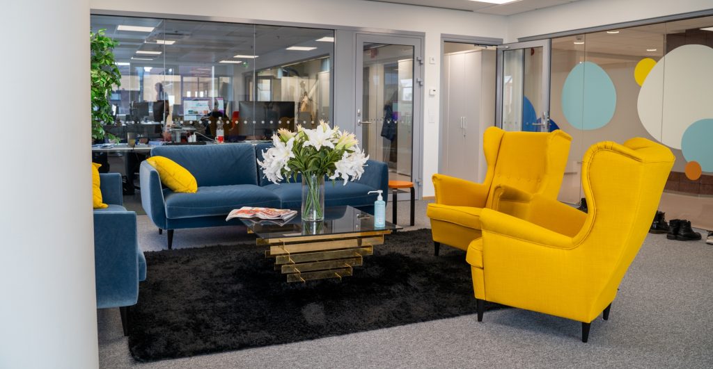 Toimiston lounge-tila, jossa on sohvia, nojatuoleja, matto ja lasipöytä kukka-asetelmalla.