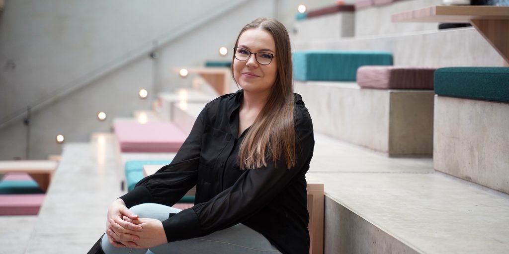 Henkilö istuu porrastetussa sisätilassa pehmeästi verhoilluilla askelmilla, valaistus korostaa portaita.