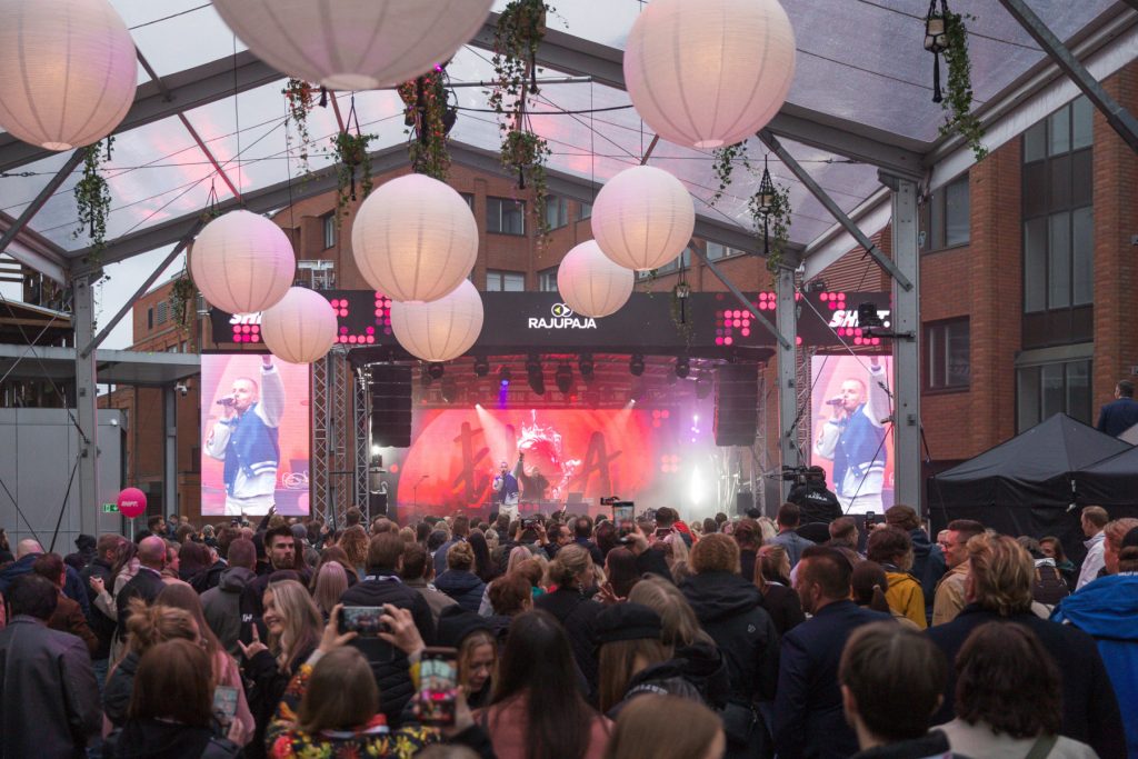 En fullsatt publik följer en live-presentation på SHIFT Business Festivals scen, med belysning och scenutrustning hängande ovanför.