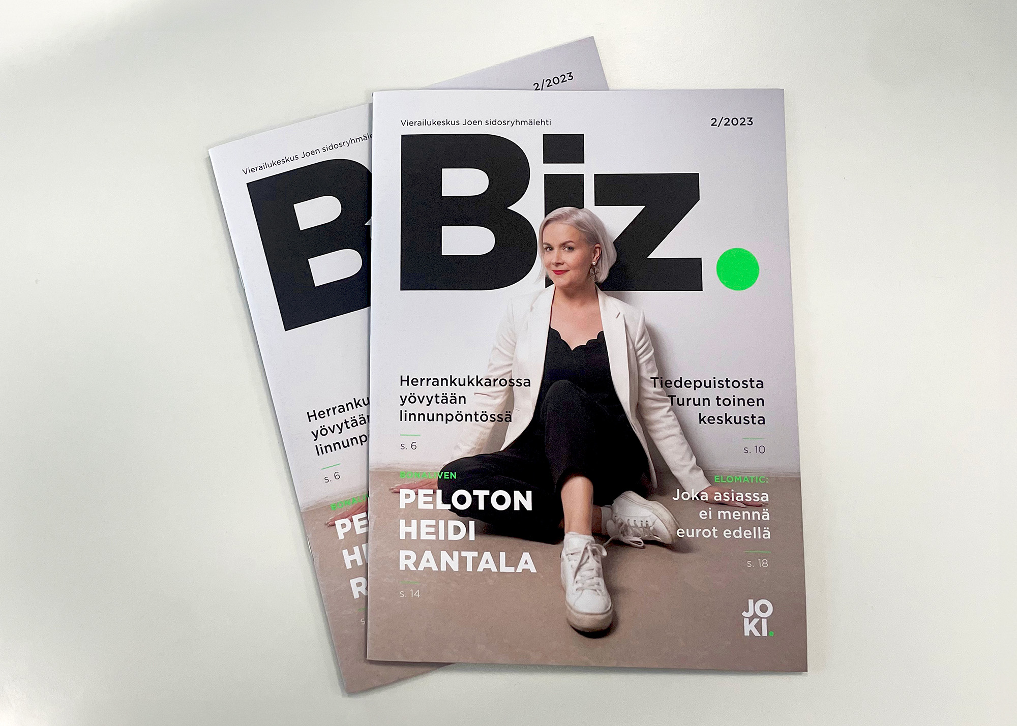 Two Biz magazines stacked on top of each other, with a person posing on the cover while sitting on the floor
