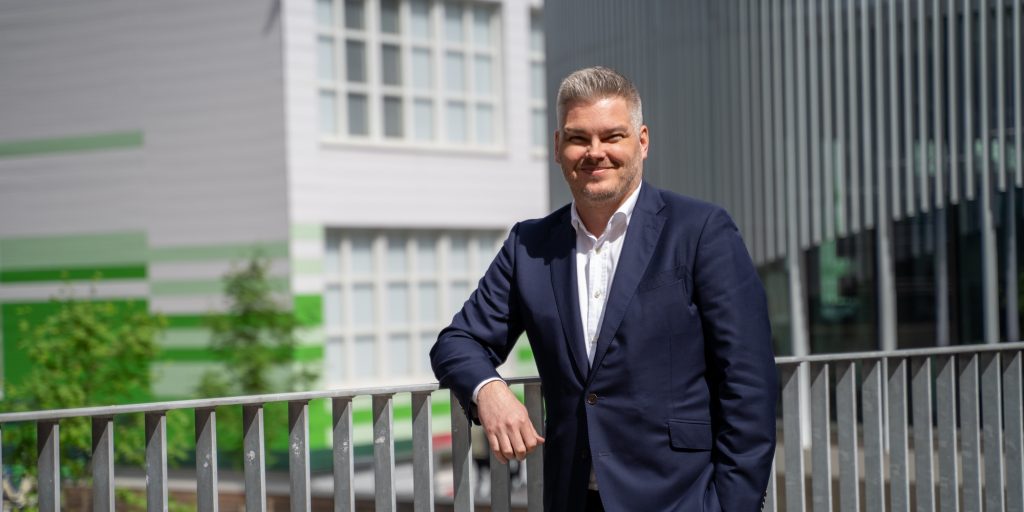 Ulkotilassa seisova henkilö kaidetta vasten modernien rakennusten edustalla.