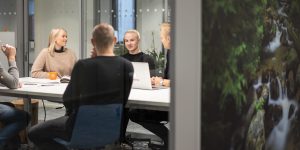 Ett möte i ett konferensrum, flera personer sitter vid ett bord med bärbara datorer och anteckningar.